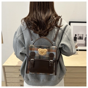 Detail of plaid backpack featuring a plush bear patch and vintage leather buckles