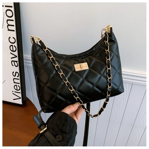 Detail of black quilted shoulder bag with gold twist lock and chain strap on table
