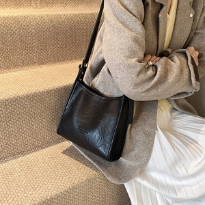 Minimalist black tote bag with vintage texture and adjustable strap worn on shoulder