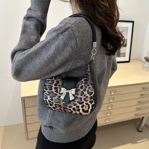 Leopard print crescent shoulder bag with silver bow accent worn by a model in a warm room
