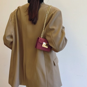 Mini burgundy suede shoulder bag with gold chain strap worn over a camel wool blazer