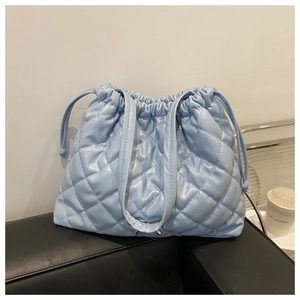 Detail of light blue quilted bucket bag with drawstring closure on a leather seat