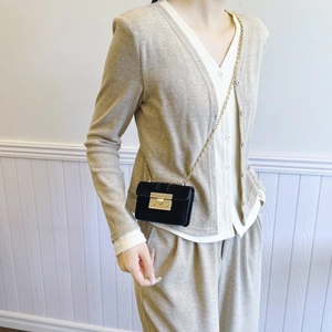 Minimalist black mini crossbody bag with gold chain strap worn by model on beige outfit