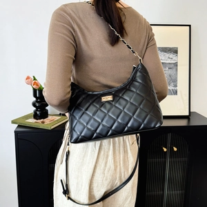 Quilted black hobo shoulder bag with gold chain strap and metal clasp on a model