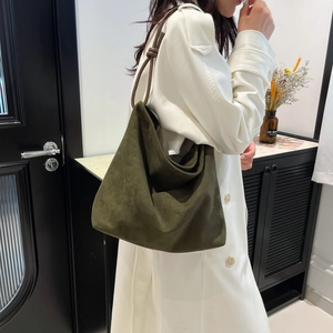Olive green suede Hobo tote bag with brown leather straps worn by model in white coat