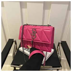Détail du sac bandoulière matelassé rose avec logo S en métal et pompon sur une chaise