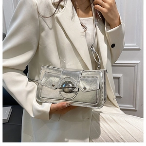 Détail du sac bandoulière argenté métallique avec fermoir rond sur un blazer blanc cassé