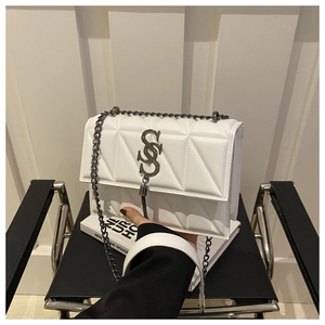 Détail d'un sac bandoulière blanc matelassé avec logo métallique et chaîne sur une chaise design