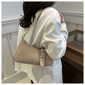 Side view of a woman wearing a beige baguette shoulder bag with silver buckle details