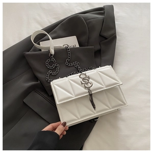 Detail of white quilted crossbody bag featuring metal SS logo and tassel on a grey blazer