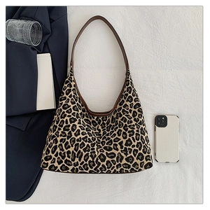 Flat lay of large leopard print hobo bag with brown leather strap on white fabric