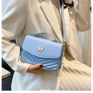 Détail du sac à bandoulière bleu clair avec fermoir papillon et texture matelassée