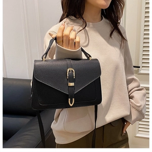 Detail of black lychee grain leather crossbody bag with golden buckle and top handle