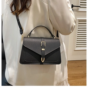 Detail of black lychee grain leather handbag with gold horseshoe buckle on white blazer
