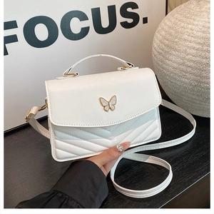 Détail du sac blanc avec décoration papillon dorée et texture matelassée en V chic