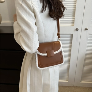 Brown leather crossbody bag with white sherpa trim styled on a white wool coat