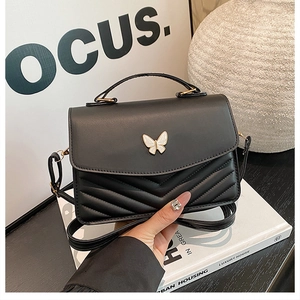 Détail du sac bandoulière noir avec fermoir papillon en émail blanc et matelassage chevron