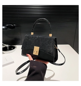 Close-up of a black leather handbag featuring a glittery flap and golden swivel clasp