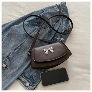 Detail of dark brown semi-circular crossbody bag with silver bow ornament on denim