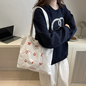 White corduroy tote bag with red letter embroidery shown in a modern lifestyle setting