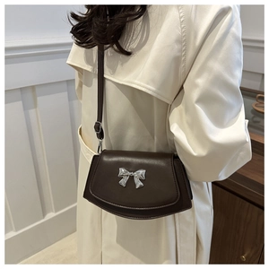 Detail of dark brown leather crossbody bag with silver bow accent on beige trench coat