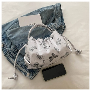Detail of white pleated handbag with butterfly print and cylindrical handle on a soft background