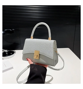 Macro detail of glossy glitter flap and golden twist lock on light grey shoulder bag