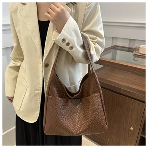Detailed texture of brown woven hobo bag carried by model in casual indoor setting
