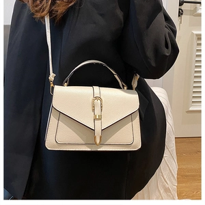 Detail view of cream-colored pebble leather crossbody bag with gold buckle and top handle