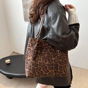 Large leopard print tote bag with brown leather straps shown on a model in a modern room