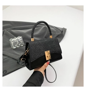Detail of black mini crossbody bag featuring a glittery top handle and golden twist lock
