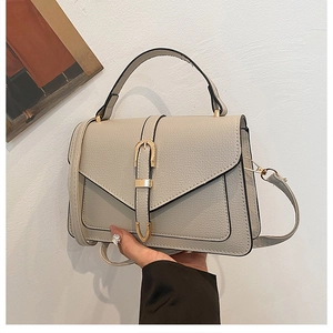 Close-up of beige lychee grain leather handbag with gold buckle and flap closure