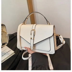 Detail of creamy white litchi pattern leather on a crossbody bag with gold buckle hardware