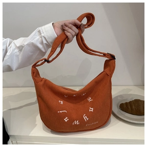 Detailed embroidery of white letters on an orange corduroy crescent shoulder bag