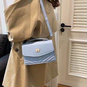 Sac bandoulière matelassé bleu ciel avec fermoir papillon porté par un mannequin