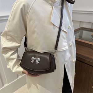 Minimalist dark brown leather crossbody bag with silver bow accent on a trench coat