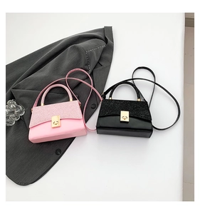 Detail of pink and black glitter square handbags with golden twist locks on a grey blazer