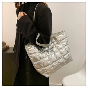Silver quilted tote bag with metallic finish and grey handles worn by a model