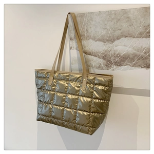 Detail view of the quilted gold puffer tote bag texture with slim leather straps