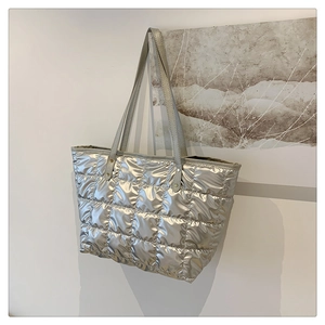 Close-up of metallic silver quilted tote bag with lattice pattern on an art gallery background