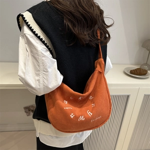 Bright orange corduroy shoulder bag with fashion lettering shown on a model