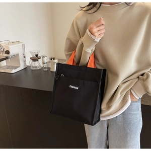 Détail du sac en toile noire avec anses orange et étiquette de mode dans un café