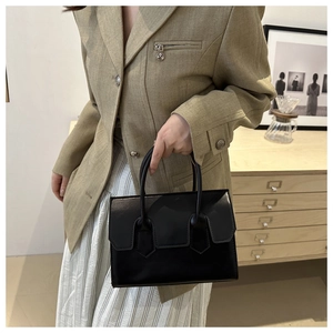 Detailed view of a sleek black patent leather handbag with a flap closure held by a model