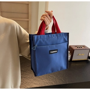 Détail du sac fourre-tout en nylon bleu avec anses rouges et poche avant zippée