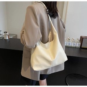 Detail of minimalist cream-colored leather tote bag with soft texture and wide shoulder strap