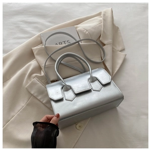 Detail view of silver rectangular handbag with metallic texture on beige suit and bedsheet