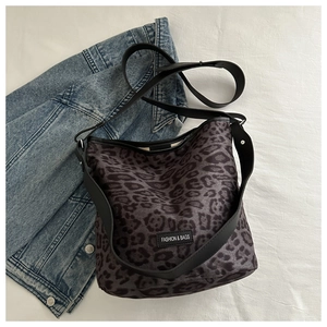 Détail d'un sac seau léopard avec une large bandoulière noire et écusson mode cousu