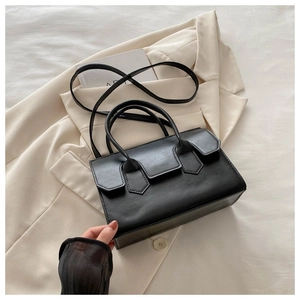 Detail view of black handbag with geometric flap decoration on top of a beige blazer