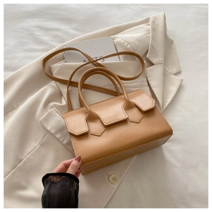 Detail of soft brown leather tote bag with unique flap design on a beige suit background