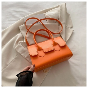 Flat lay of an orange vegan leather handbag on a beige blazer and a fashion magazine